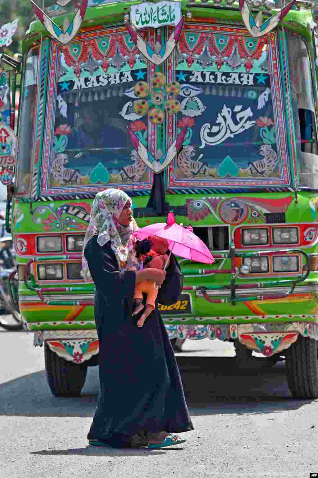 زنی هنگام عبور از خیابانی در کراچی کودک خود را زیر سایهٔ چتر گرفته است 