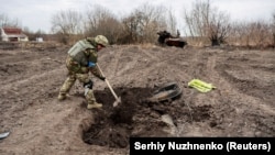 A Ukrainian serviceman buries the remains of what he said was the dead body of a Russian soldier in a village near Kyiv that was reclaimed by Ukraine in March 2022.