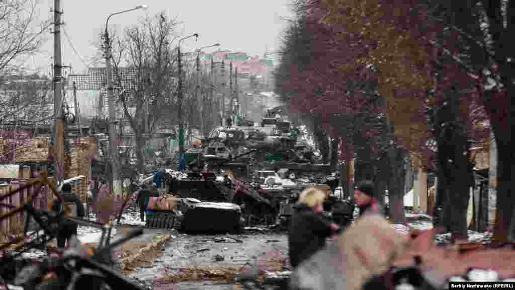 Мирные жители смотрят на уничтоженную колонну российской бронетехники в Буче, пригороде Киева, 1 марта 2022 года. Через несколько дней российские военные захватили Бучу, но меньше чем через месяц они отступили. После их ухода в Буче были собраны доказательства военных преступлений