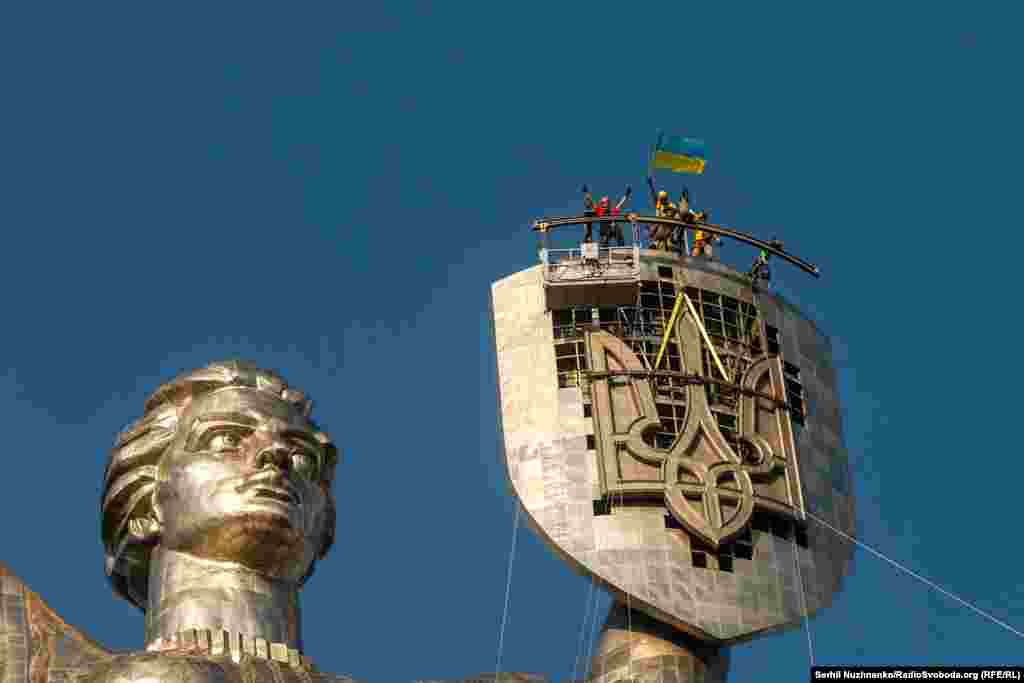 Рабочие отмечают установку украинского трезубца на щите монумента «Родина-мать» в Киеве, 6 августа 2023 года. Огромный трезубец заменил советский герб