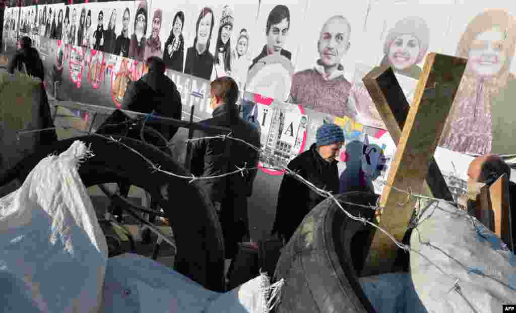 Люди проходять повз галереї портретів активістів #Євромайдан’у, наклеєних на стіну поряд з барикадою на майдані Незалежності у Києві, 24 грудня 2013 року