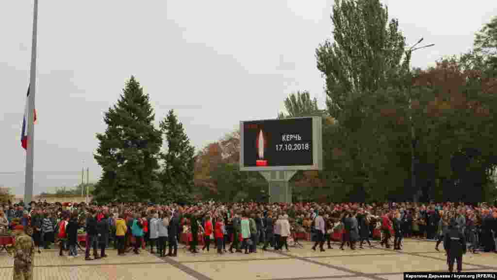 На площади Ленина стоят в ряд 17 закрытых гробов с телами жертв трагедии.Рядом с каждым из них - фотографии и таблички с именами погибших. Играет траурная музыка. На большом экране изображена свеча и надпись «Керчь 17.10.2018»