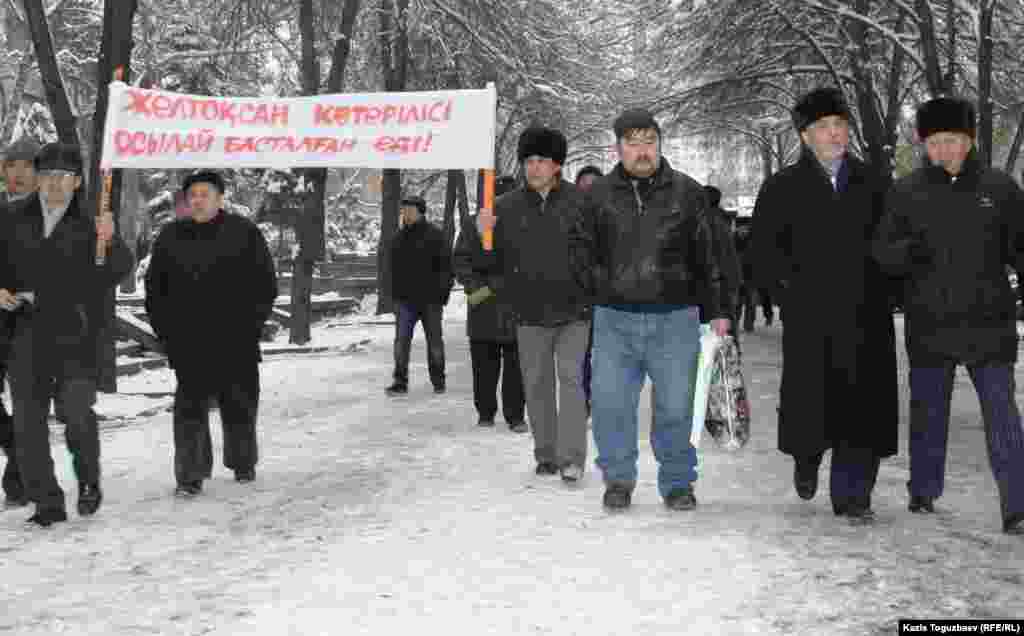 Политик Хасен Кожа-Ахмет и его сторонники идут к офису президентской партии "Нур Отан", чтобы выразить протест действиям властям в Жанаозене во время массовых беспорядков.