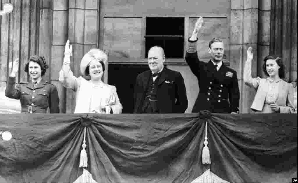 Britanski premijer Winston Churchill, na balkonu Buckinghamske palate, s kraljevskom porodicom, uz aplauz publike, Velika Britanija, 8. maj 1945. Te večeri, buduća kraljica Elizabeta II (lijevo) i princeza Margaret (desno) probijaju se kroz gomilu kako bi se pridružile zabavi. Elizabeta je opisala to iskustvo kao "jednu od najupečatljivijih noći u svom životu".