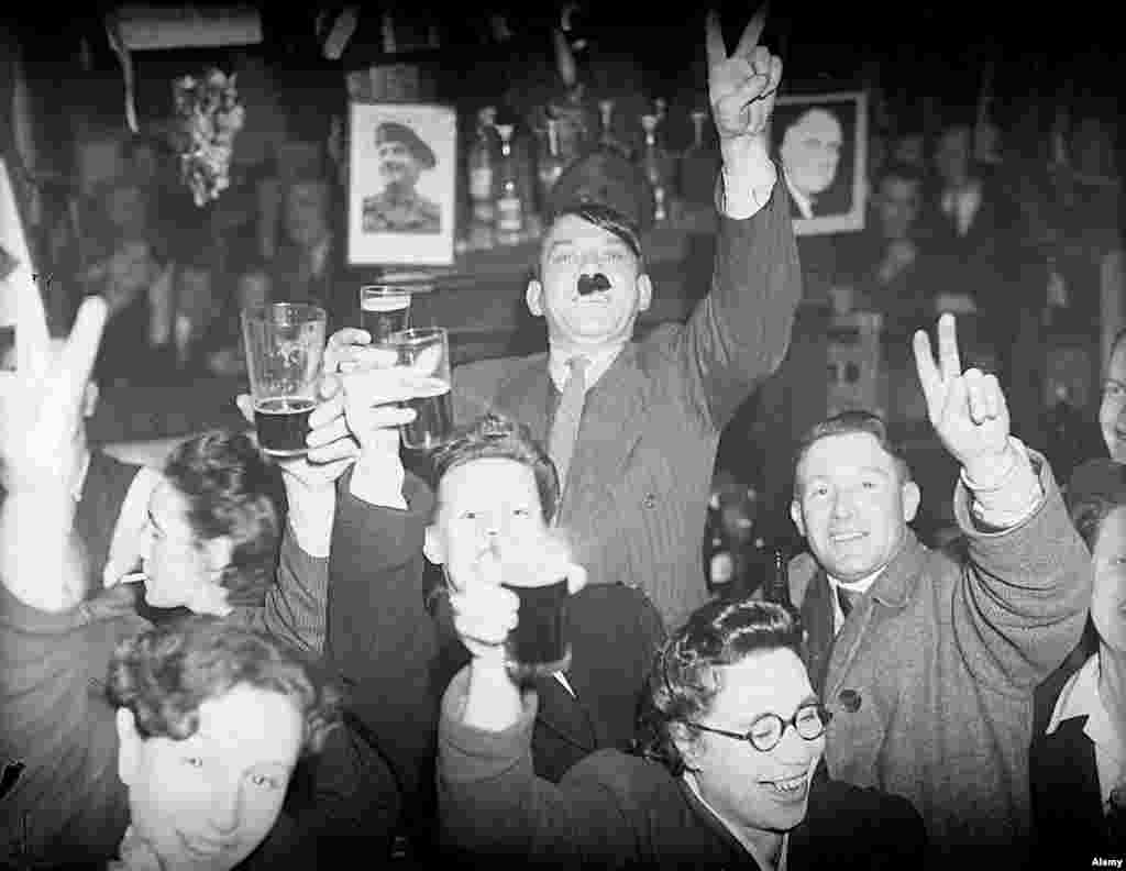 Stanovnici Londona, uključujući i muškarca s brkovima u stilu Hitlerovih, veselo nazdravljaju čašom piva u pubu u Lambethu, Ujedinjeno Kraljevstvo, 8. maj 1945.