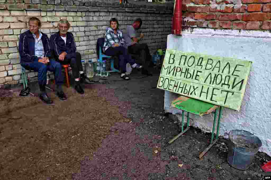 На этой фотографии, сделанной 16 августа 2024 года во время медиа-тура, организованного Украиной, изображены жители, сидящие рядом с табличкой "В подвале гражданские, военных нет" в подконтрольном Украине российском городе Суджа Курской области. 