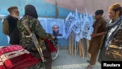 Taliban militants gather by a picture of their leader, Mullah Haibatullah Akhundzada, in Kabul, who was named supreme leader of the Taliban-led government.